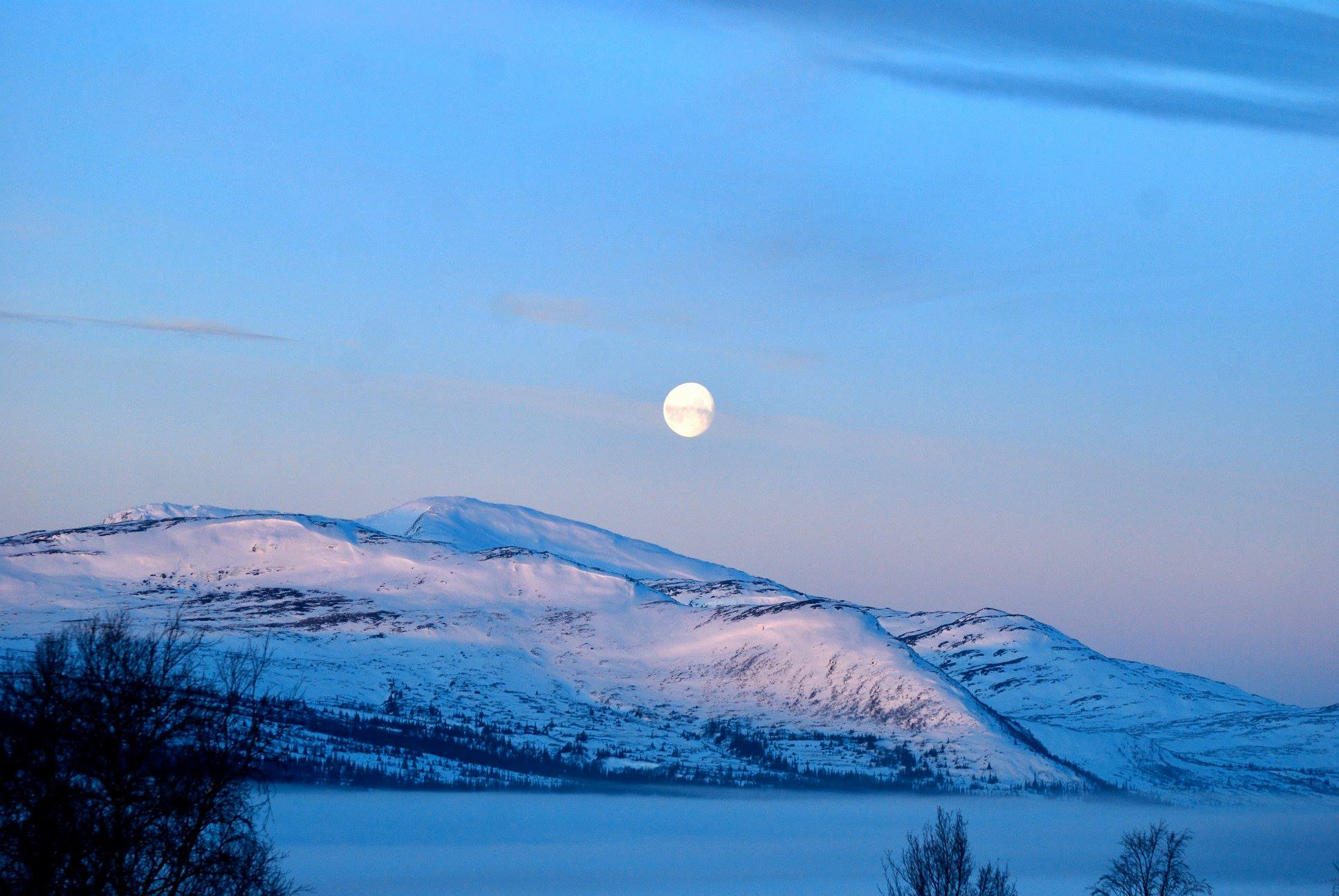 Fullmånen står högt över snötäckta fjäll