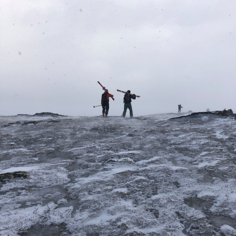 Skidåkare med skidorna över axeln, går över isig fjälltopp.